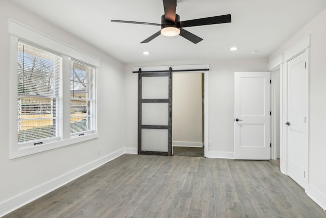 unfurnished bedroom featuring a barn door, baseboards, a ceiling fan, wood finished floors, and recessed lighting