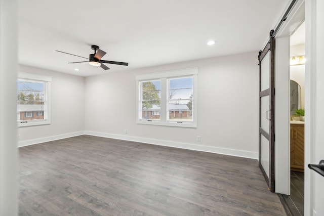 empty room with a ceiling fan, a barn door, baseboards, and dark wood-style flooring