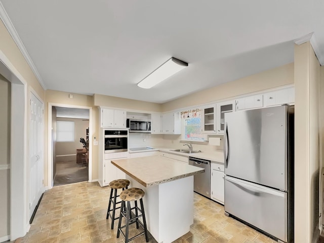 kitchen with a kitchen island, stainless steel appliances, light countertops, white cabinetry, and a sink