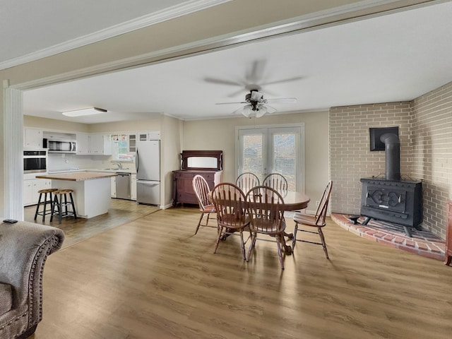 dining room featuring ceiling fan, light wood finished floors, a wood stove, and crown molding