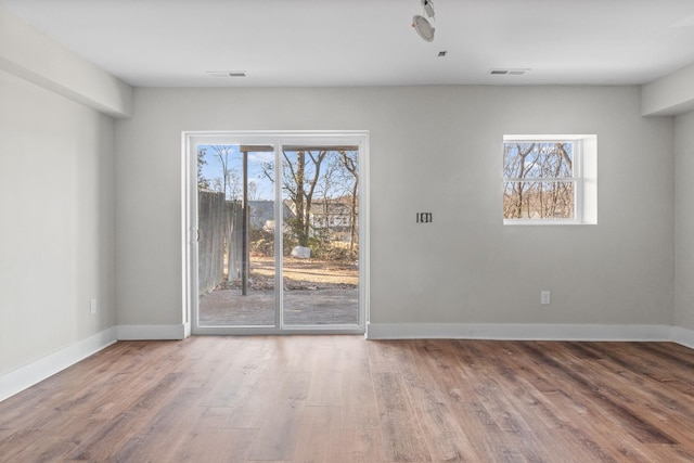 spare room featuring plenty of natural light, visible vents, baseboards, and wood finished floors