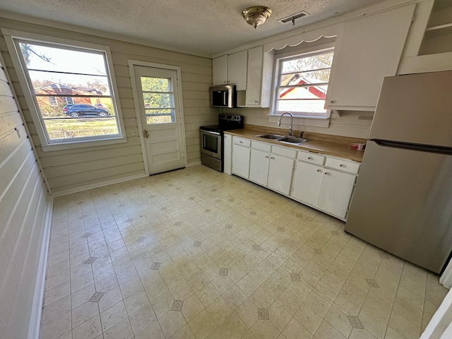 kitchen with stainless steel appliances, a sink, visible vents, white cabinets, and light floors