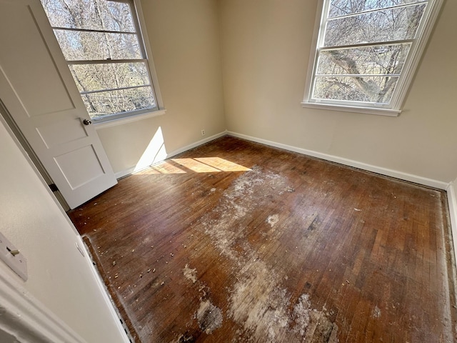 empty room featuring plenty of natural light, wood-type flooring, and baseboards