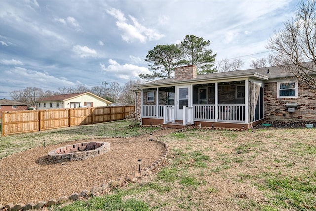 back of house with a fire pit, a sunroom, a chimney, fence, and brick siding