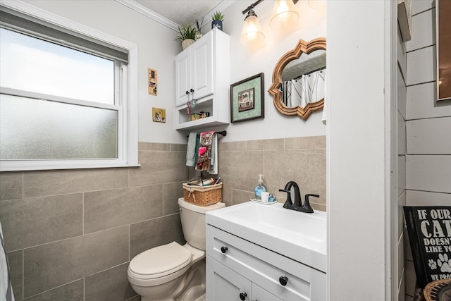 bathroom featuring toilet, a wainscoted wall, crown molding, vanity, and tile walls