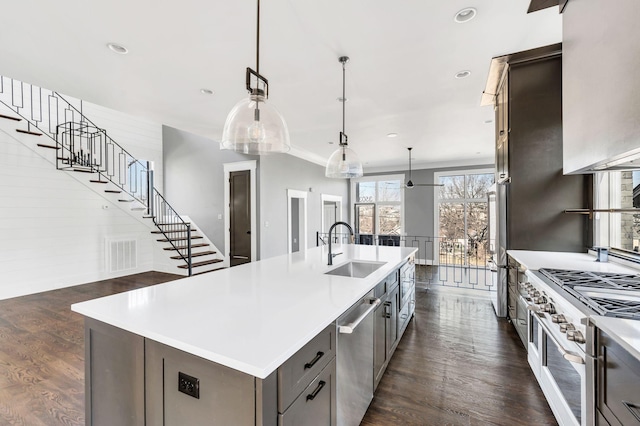 kitchen featuring a kitchen island with sink, dark wood-type flooring, a sink, light countertops, and appliances with stainless steel finishes