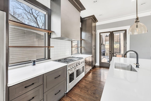 kitchen featuring a sink, wall chimney range hood, double oven range, dark wood-style floors, and tasteful backsplash