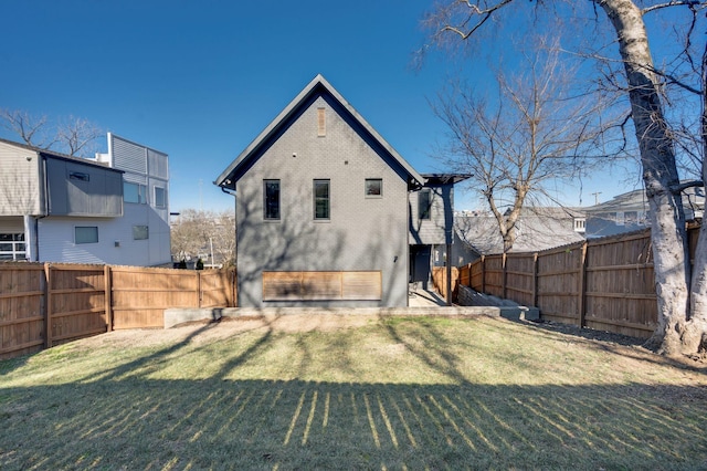 rear view of property featuring brick siding, a fenced backyard, and a yard