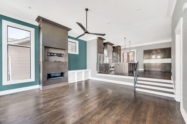 unfurnished living room featuring dark wood-style flooring, crown molding, visible vents, a ceiling fan, and a glass covered fireplace