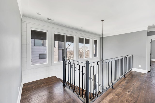 hallway with baseboards, visible vents, ornamental molding, wood finished floors, and an upstairs landing