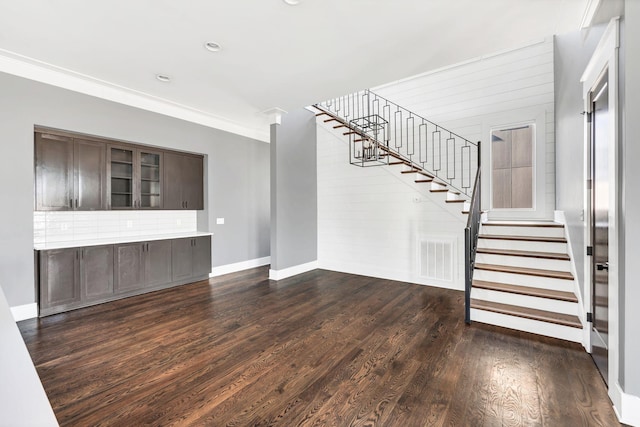 unfurnished living room with dark wood-style flooring, visible vents, baseboards, stairway, and crown molding