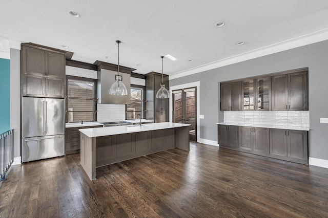 kitchen with high quality fridge, dark wood-type flooring, light countertops, dark brown cabinets, and glass insert cabinets