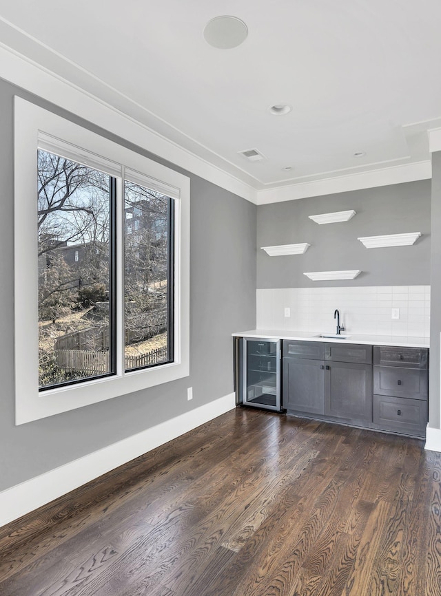 bar with beverage cooler, baseboards, visible vents, dark wood-style flooring, and a sink