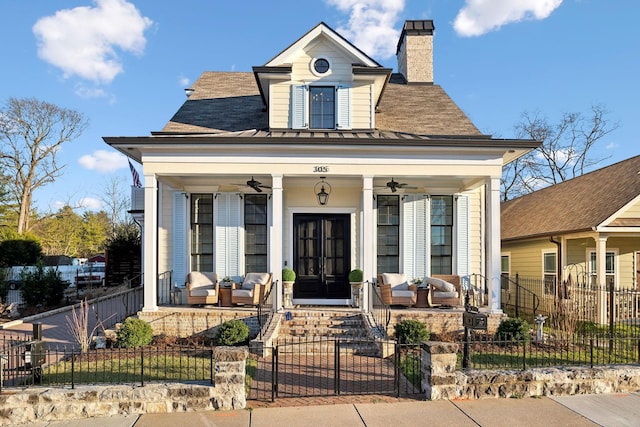 view of front of house with a ceiling fan, a fenced front yard, a chimney, covered porch, and french doors