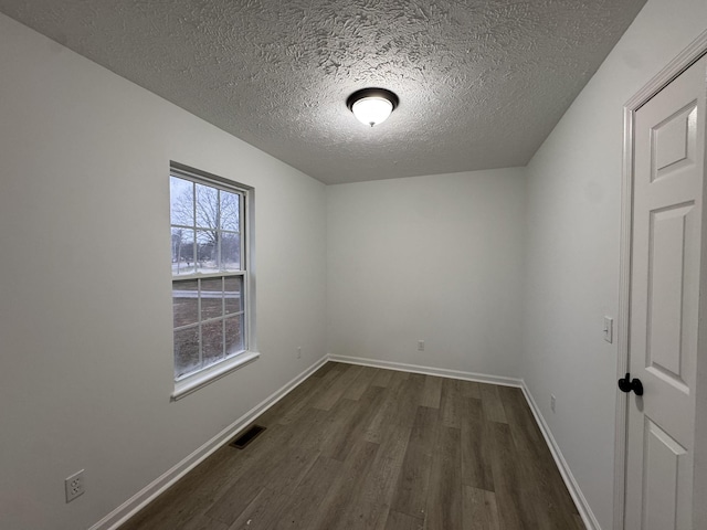 spare room featuring baseboards, visible vents, dark wood finished floors, and a textured ceiling