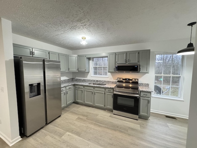 kitchen featuring light stone counters, gray cabinetry, appliances with stainless steel finishes, a sink, and light wood-type flooring