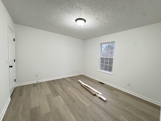 empty room featuring visible vents, a textured ceiling, baseboards, and wood finished floors