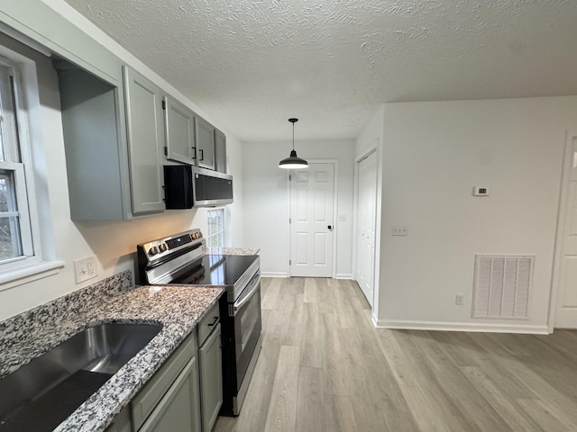 kitchen featuring stainless steel appliances, visible vents, a sink, light stone countertops, and light wood-type flooring