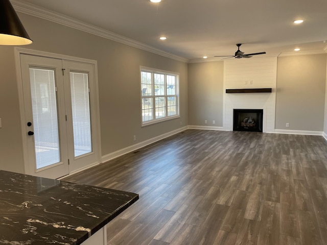 unfurnished living room with a large fireplace, baseboards, a ceiling fan, dark wood-style flooring, and crown molding