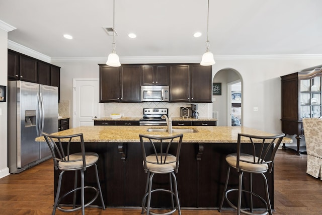 kitchen with arched walkways, appliances with stainless steel finishes, dark wood-style flooring, and light stone counters