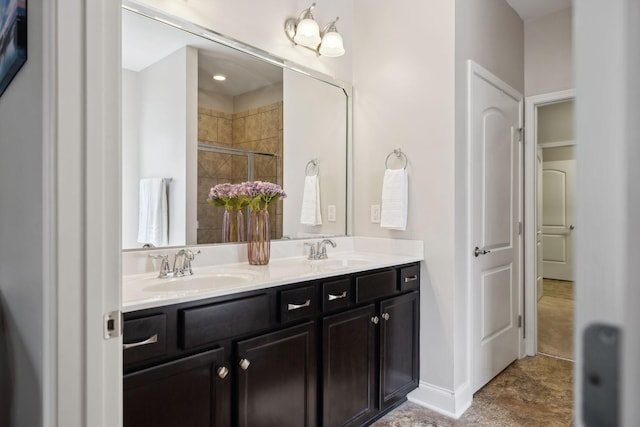 bathroom with double vanity, a shower stall, baseboards, and a sink