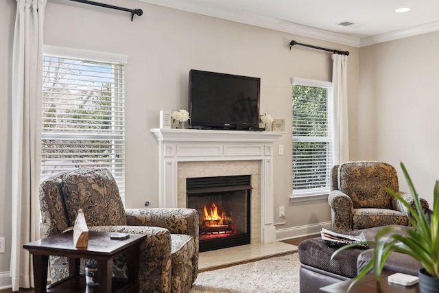 living area featuring a premium fireplace, wood finished floors, visible vents, baseboards, and ornamental molding