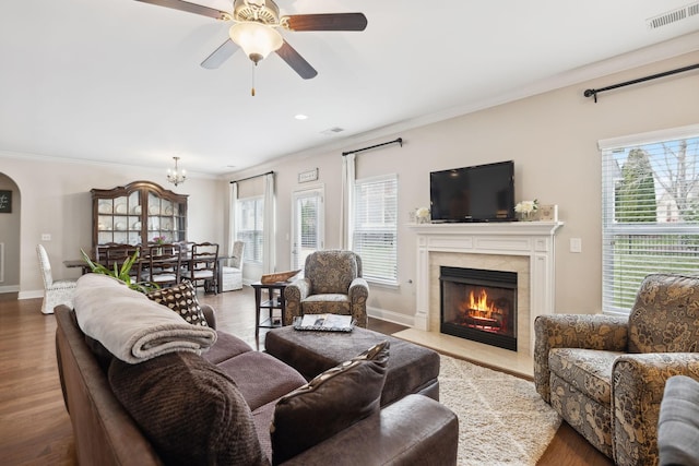 living room with visible vents, arched walkways, a premium fireplace, wood finished floors, and crown molding