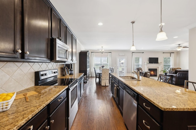 kitchen featuring stainless steel appliances, decorative backsplash, dark wood-type flooring, a sink, and a warm lit fireplace