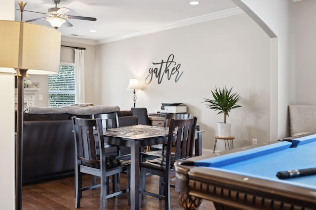 dining room featuring arched walkways, ceiling fan, a fireplace, wood finished floors, and crown molding