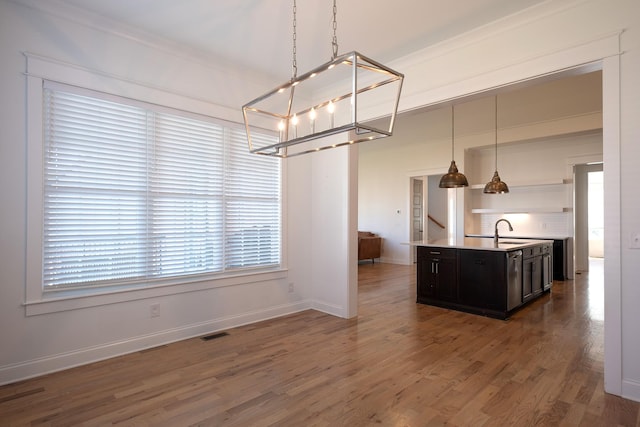 kitchen with a center island with sink, visible vents, wood finished floors, hanging light fixtures, and a sink