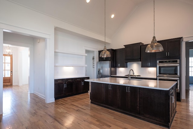 kitchen featuring open shelves, stainless steel appliances, light countertops, and an island with sink