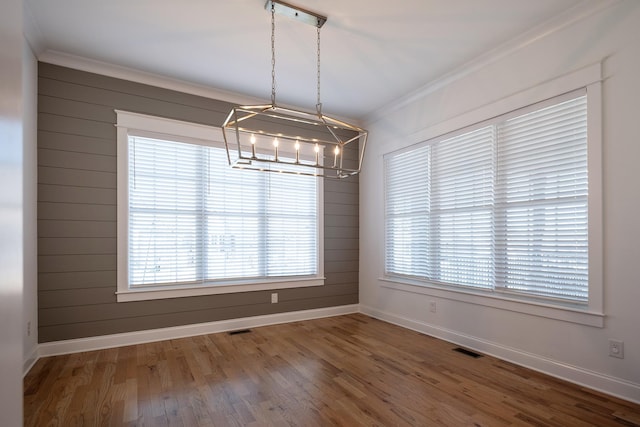 unfurnished dining area with baseboards, visible vents, crown molding, and wood finished floors