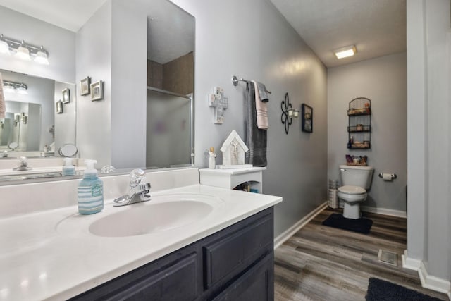 bathroom featuring a stall shower, baseboards, toilet, wood finished floors, and vanity