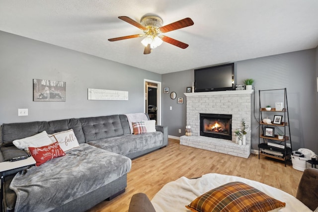 living room featuring a brick fireplace, ceiling fan, a textured ceiling, wood finished floors, and baseboards