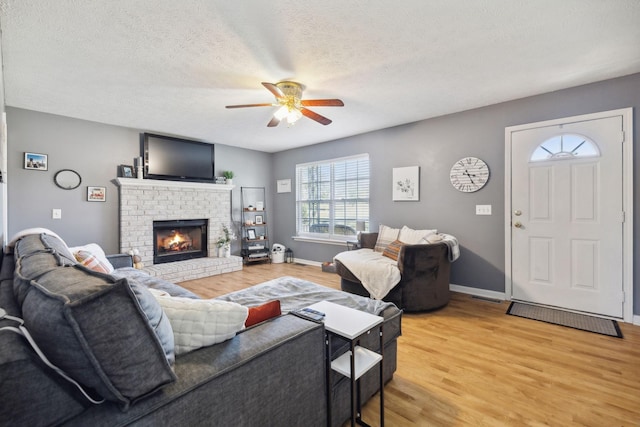 living room featuring a ceiling fan, light wood-type flooring, a fireplace, and a textured ceiling