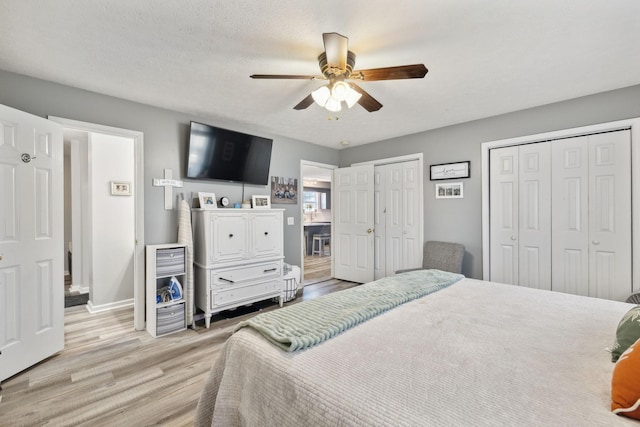 bedroom featuring two closets, a ceiling fan, a textured ceiling, wood finished floors, and baseboards