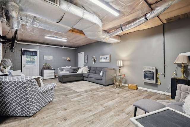 living area featuring concrete block wall, baseboards, wood finished floors, heating unit, and a wood stove