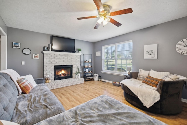 living room with baseboards, ceiling fan, wood finished floors, a textured ceiling, and a fireplace