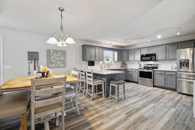 kitchen with gray cabinetry, a peninsula, appliances with stainless steel finishes, light wood-type flooring, and tasteful backsplash