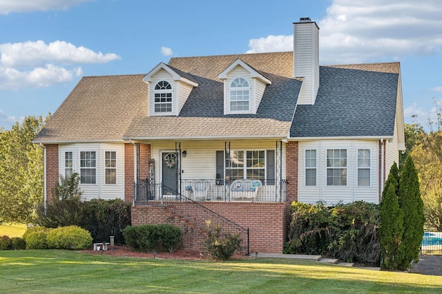 new england style home featuring a porch, brick siding, a shingled roof, and a front lawn