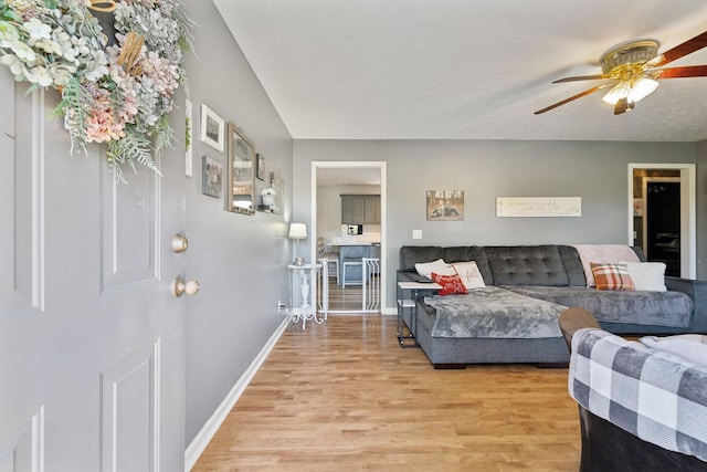 living area featuring light wood finished floors, baseboards, and a ceiling fan