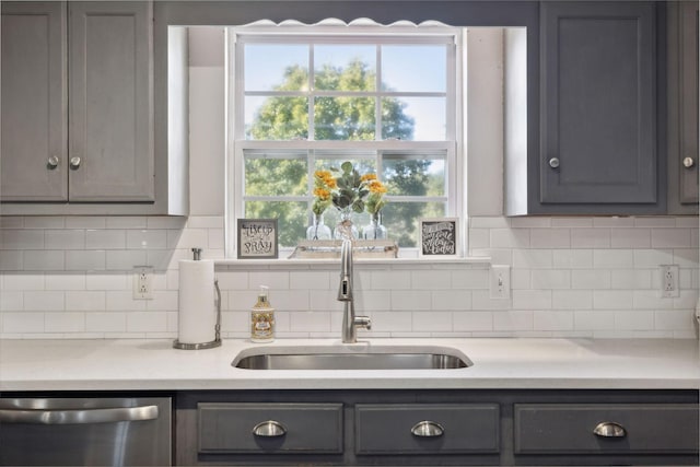 kitchen with a sink, light countertops, gray cabinets, dishwasher, and tasteful backsplash