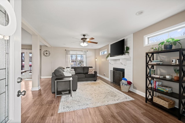 living room featuring a large fireplace, plenty of natural light, baseboards, and wood finished floors