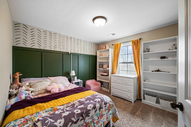 bedroom with a textured ceiling, a wainscoted wall, carpet floors, visible vents, and wallpapered walls