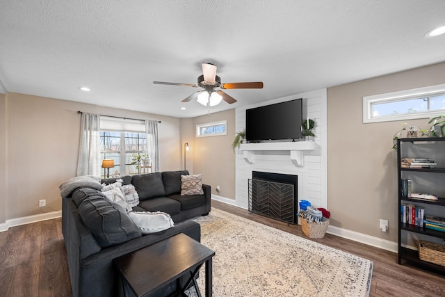 living room featuring dark wood-style floors, a fireplace, plenty of natural light, and baseboards