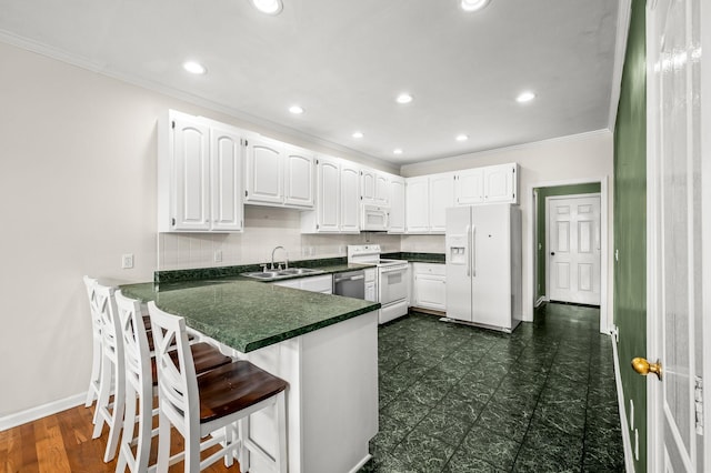 kitchen featuring dark countertops, white cabinets, a sink, white appliances, and a peninsula