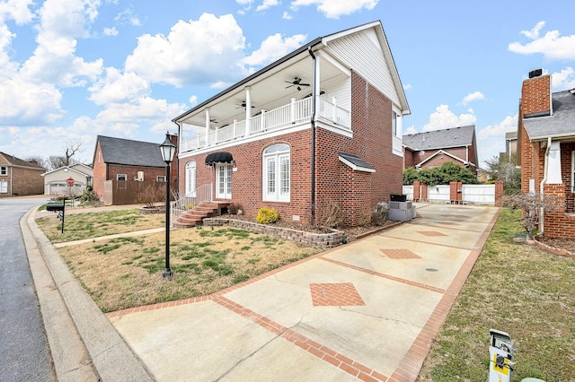 view of front of house with brick siding, a ceiling fan, a balcony, central air condition unit, and a front yard