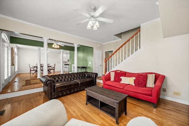 living area with decorative columns, wood-type flooring, ornamental molding, ceiling fan, and stairs