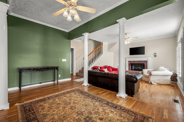 living room featuring wood finished floors, visible vents, a ceiling fan, stairs, and decorative columns