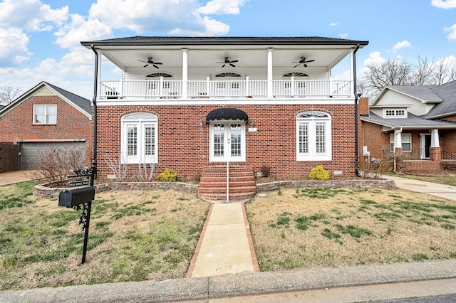 view of front facade featuring a balcony, brick siding, a front yard, and french doors